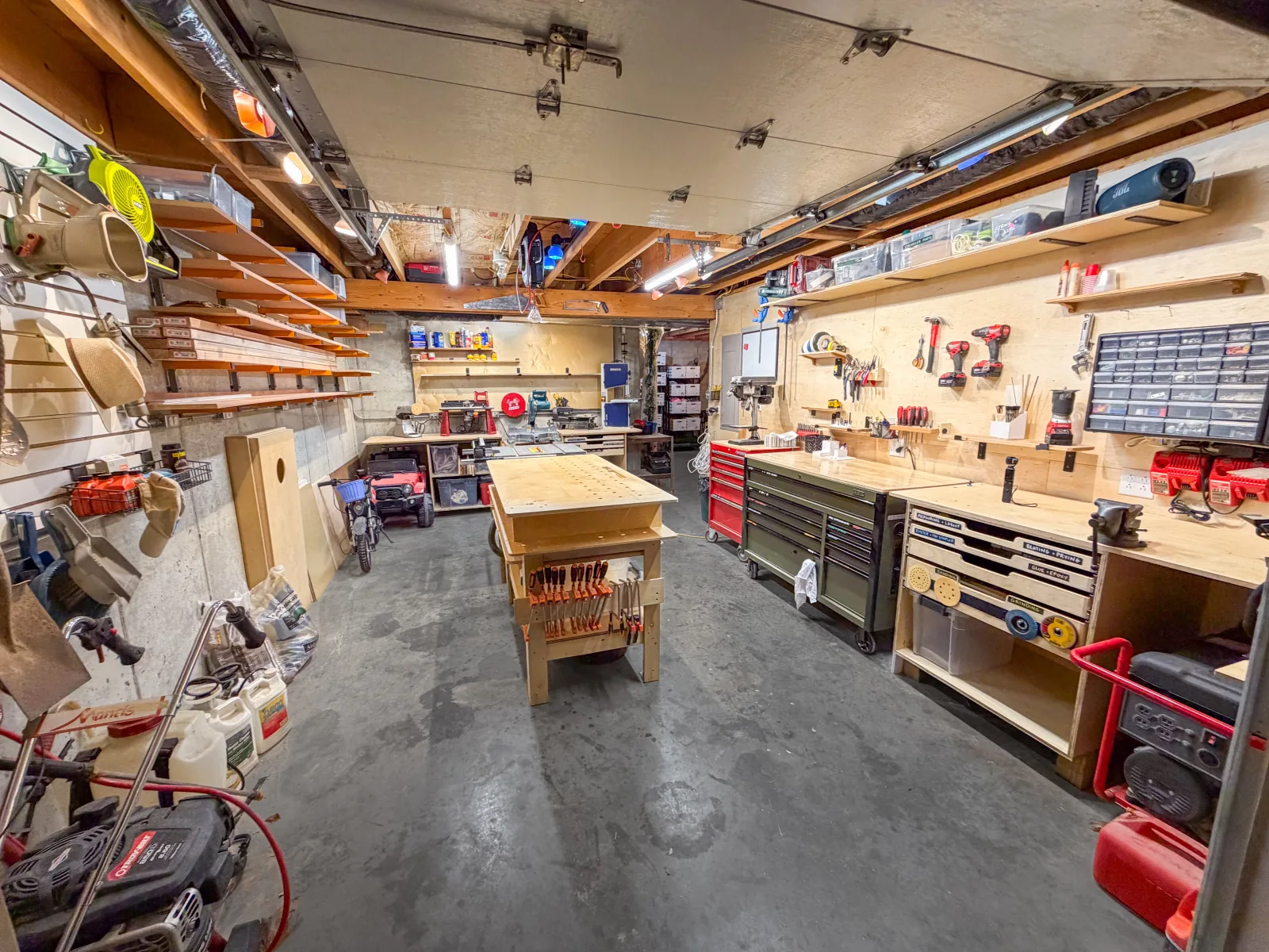 Jim&rsquo;s finished 12 by 20 workshop: lumber racks, a central workbench, and accessible tools around an open walkway